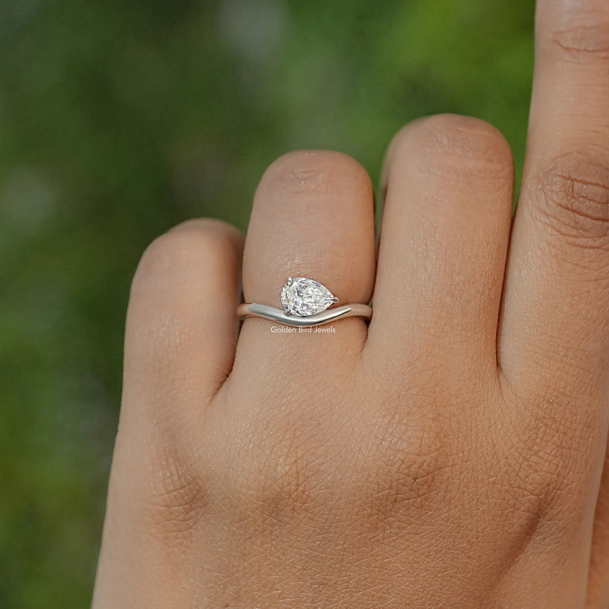 Pear-cut moissanite solitaire ring on finger with slim metallic band