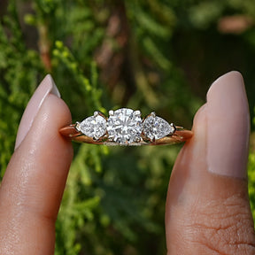 Front View of Pear And Round Cut Lab Diamond Three Stone Ring In two Fingers