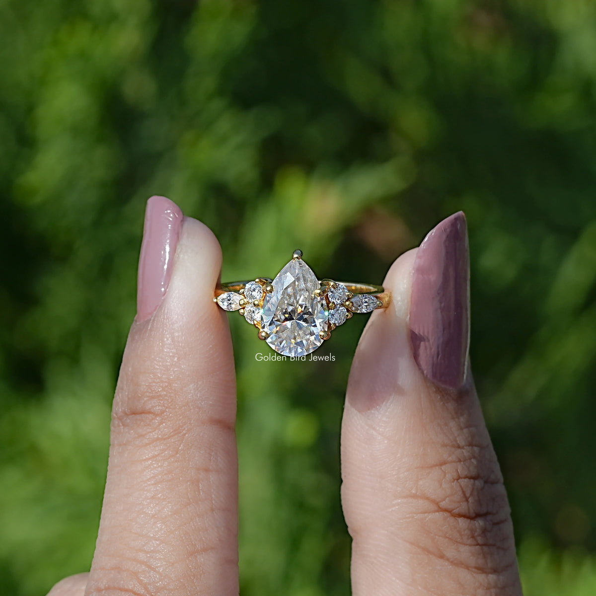 Front view of Pear cut moissanite Accent engagement ring in two fingers 