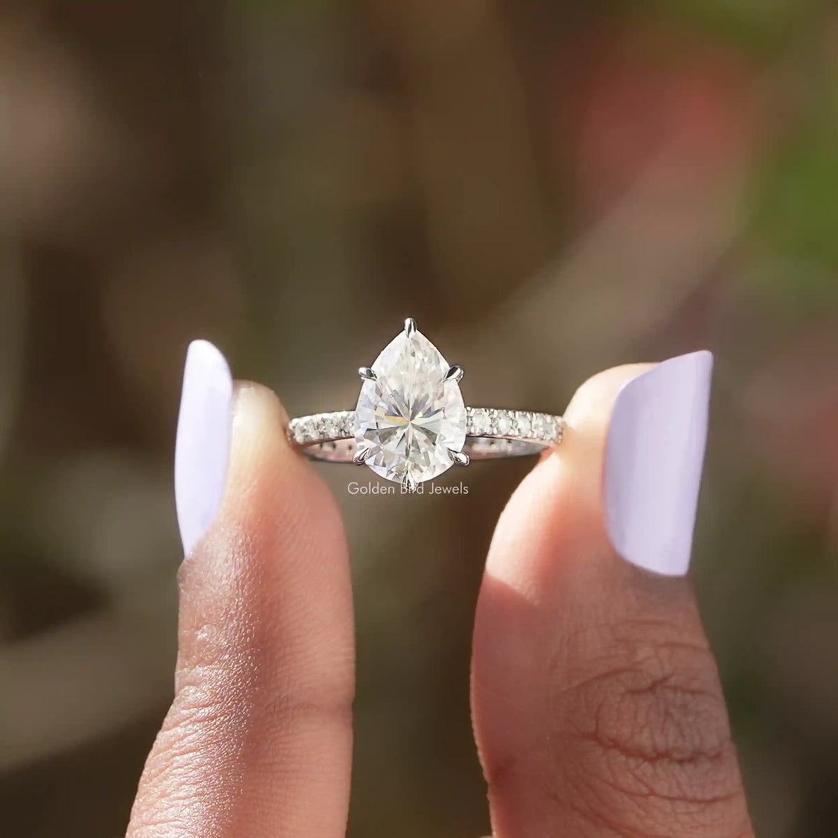 [In two finger front view of pear cut moissanite accent stone ring in 14k white gold]-[Golden Bird Jewels]