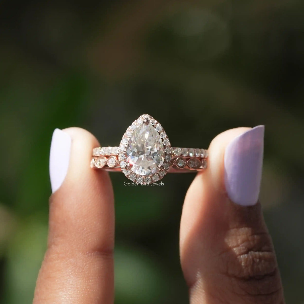 Two fingers holding the Pear Cut Moissanite Halo Bridal Ring Set