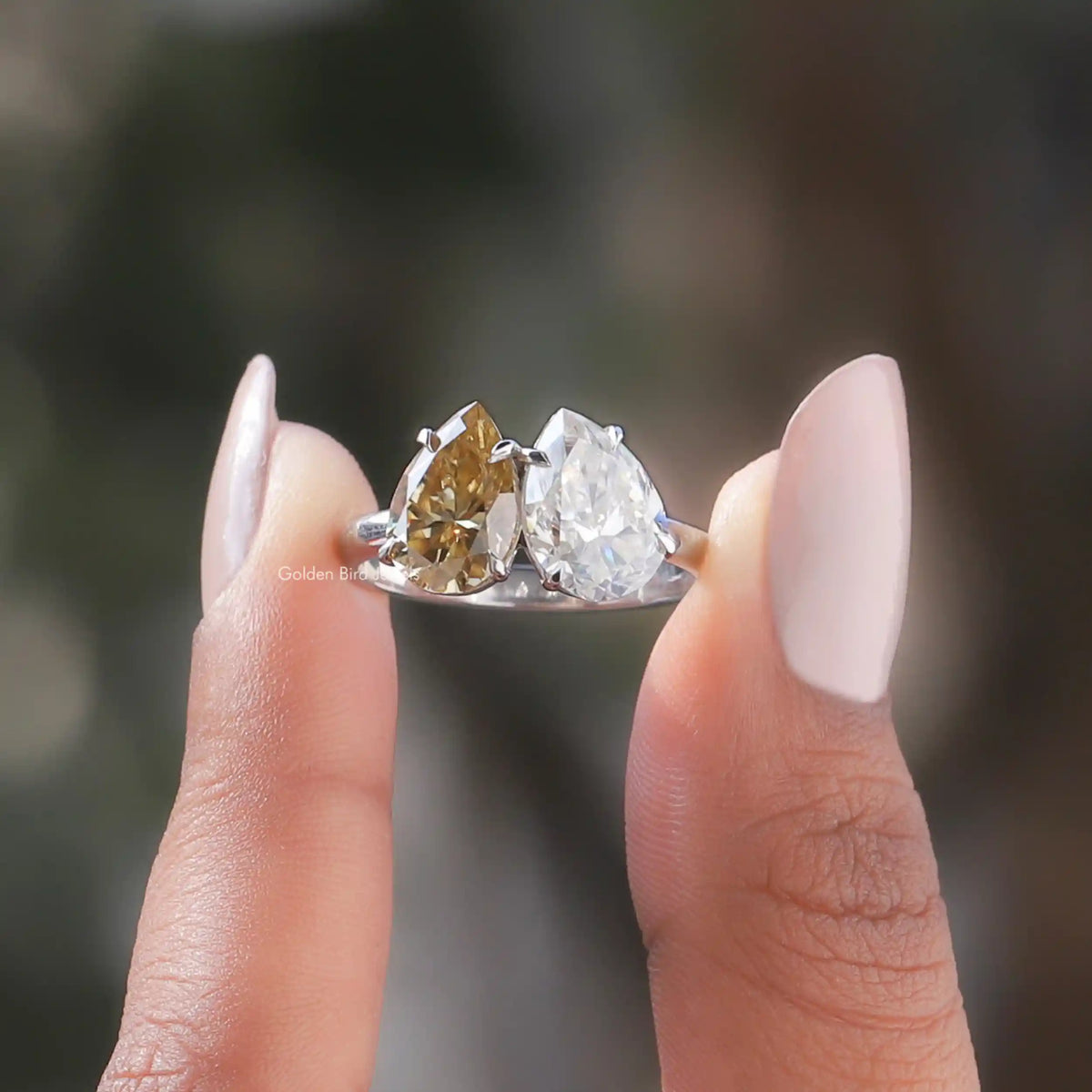 Two fingers holding the Yellow And Colorless Pear Cut Moissanite Toi Et Moi Ring