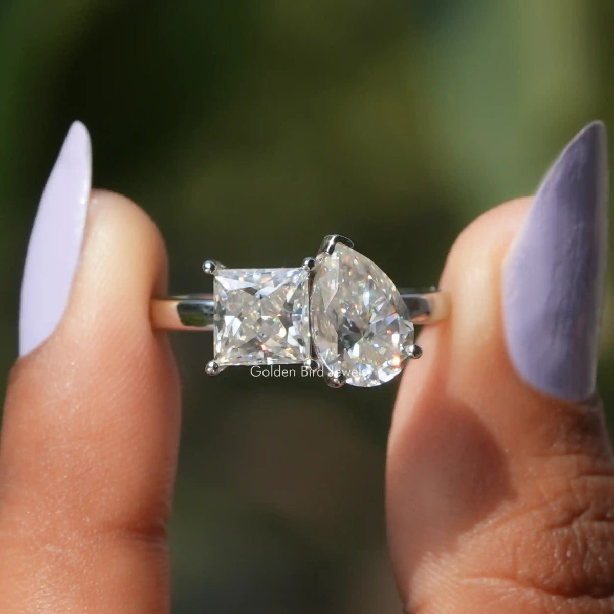 Two fingers holding the Pear And Princess Cut Moissanite Toi Et Moi Ring