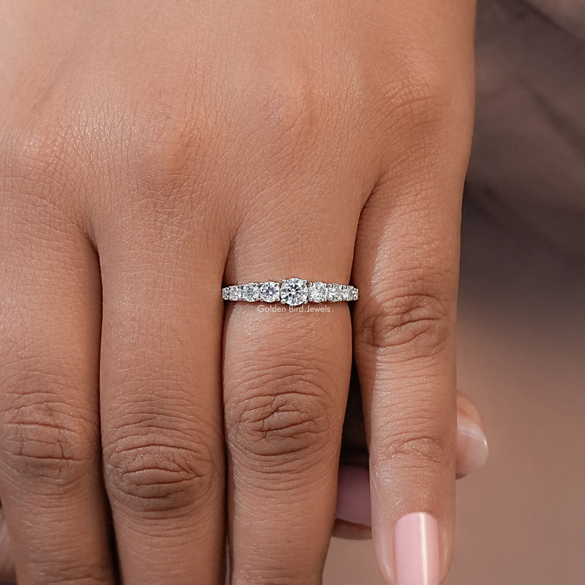 Silver-toned moissanite engagement ring with round-stone band worn on hand