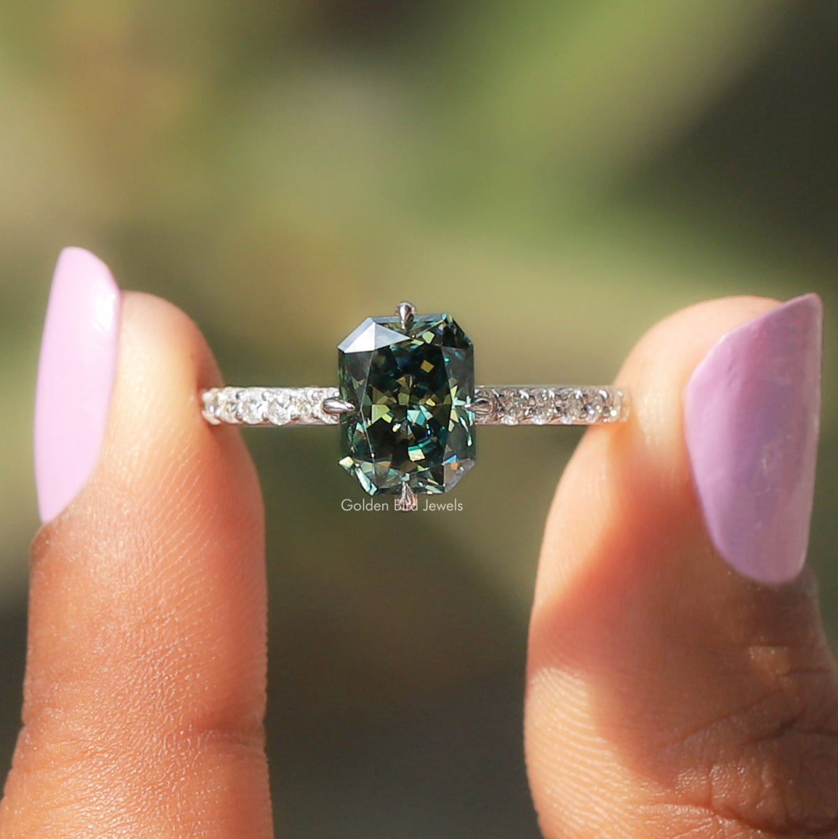 [In two finger front view of green radiant cut accent stone moissanite ring]-[Golden Bird Jewels]
