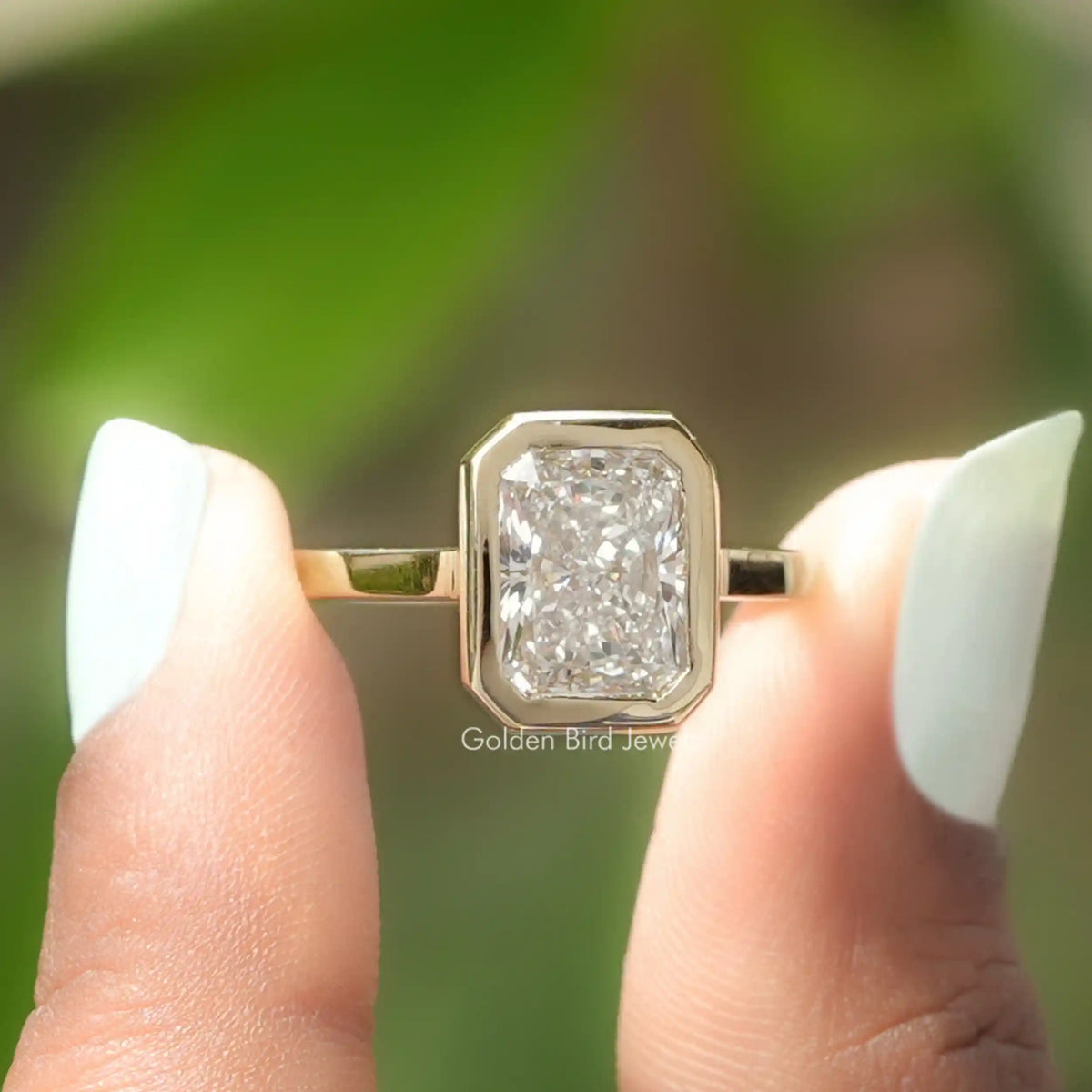 Two fingers holding the Radiant Cut Diamond Bezel Set Solitaire Ring