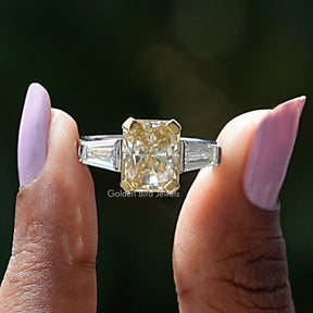 Two fingers holding the Radiant Cut Three Stone Moissanite Ring