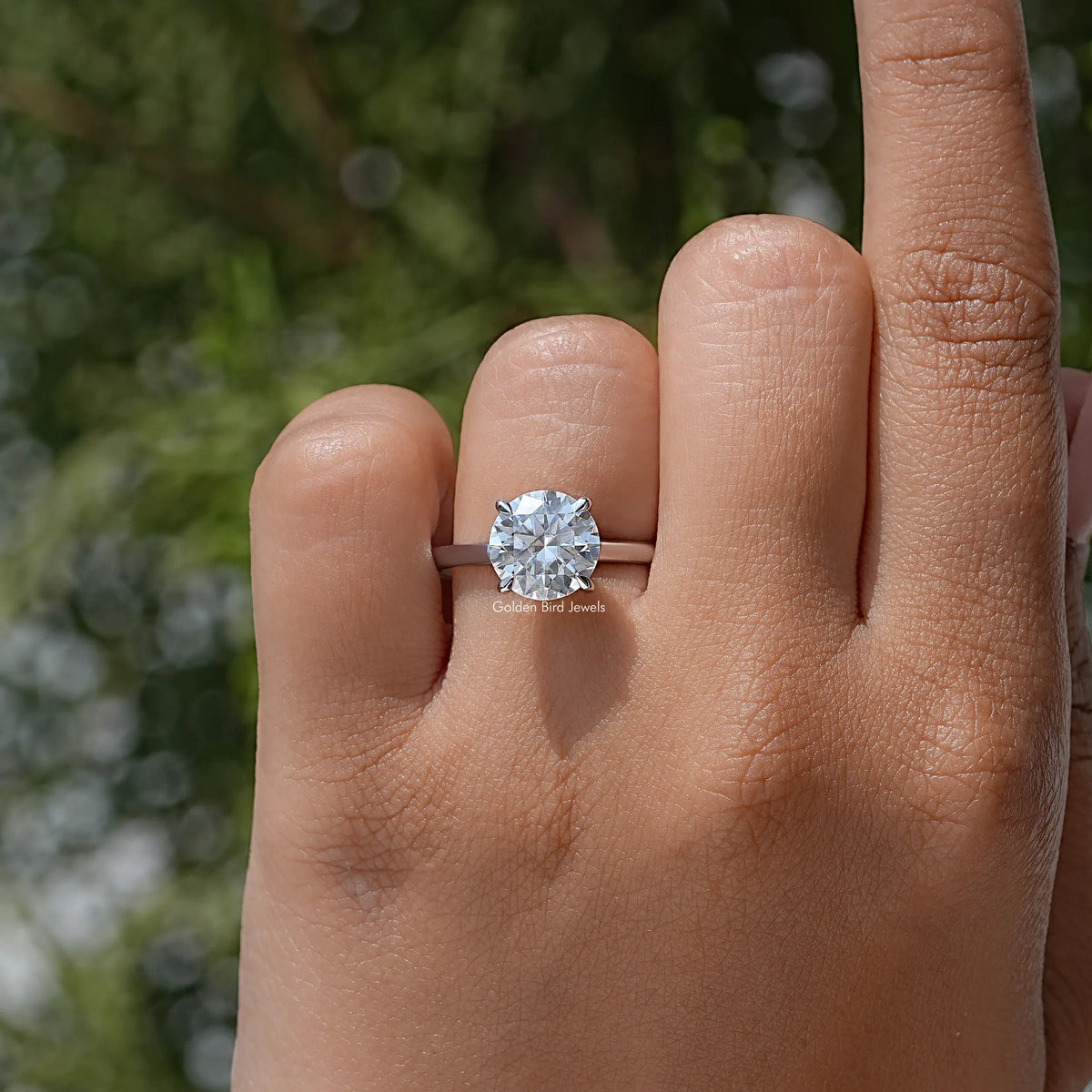 Round solitaire moissanite engagement ring on finger, featuring a bright round center stone
