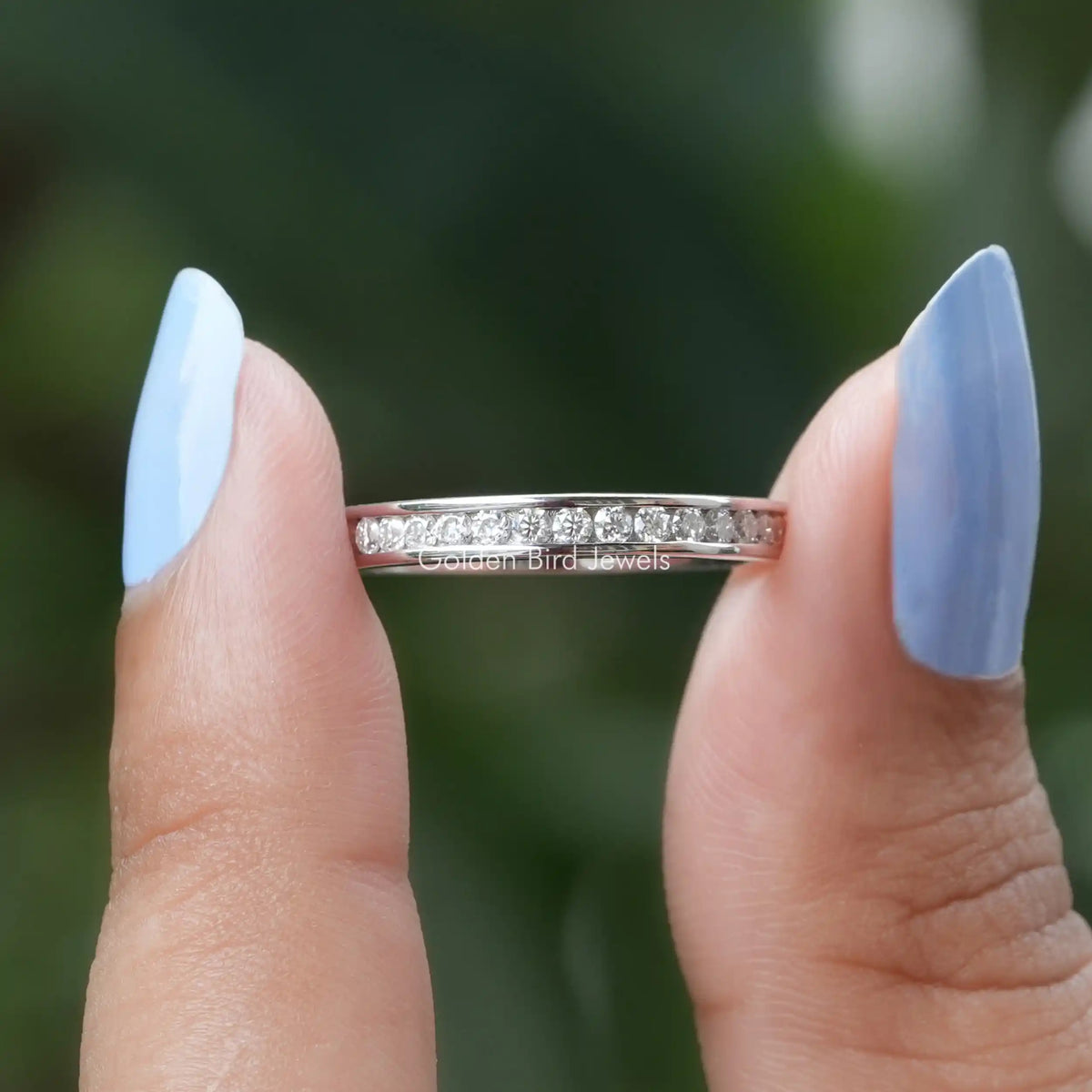 Two fingers holding the Round Cut Moissanite Channel Set Eternity Wedding Band