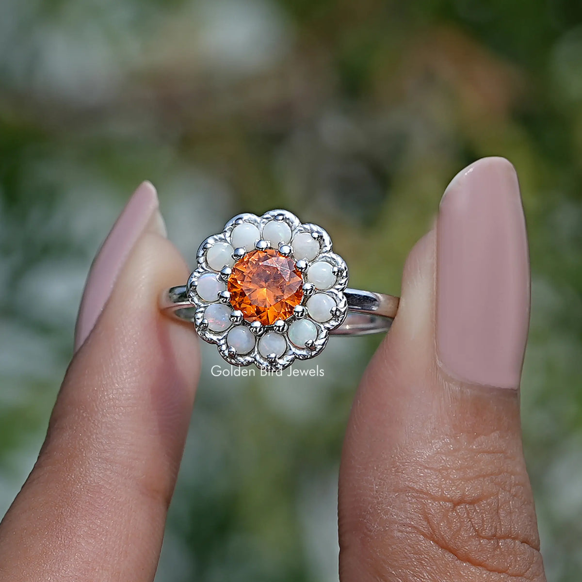 Two fingers holding the Round Cut Sunstone Halo Engagement Ring