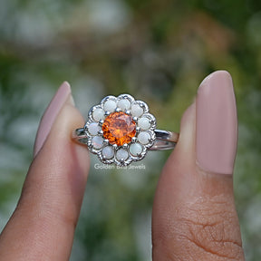 Two fingers holding the Round Cut Sunstone Halo Engagement Ring