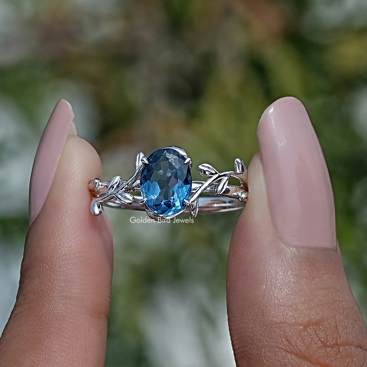 Two fingers holding the Blue Oval Cut Gemstone Engagement Ring