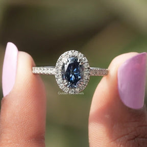 Two fingers holding the Sapphire Blue Oval Cut Halo Engagement Ring