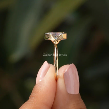 Side View of Emerald Cut Half Bezel Set Engagement Ring In two fingers