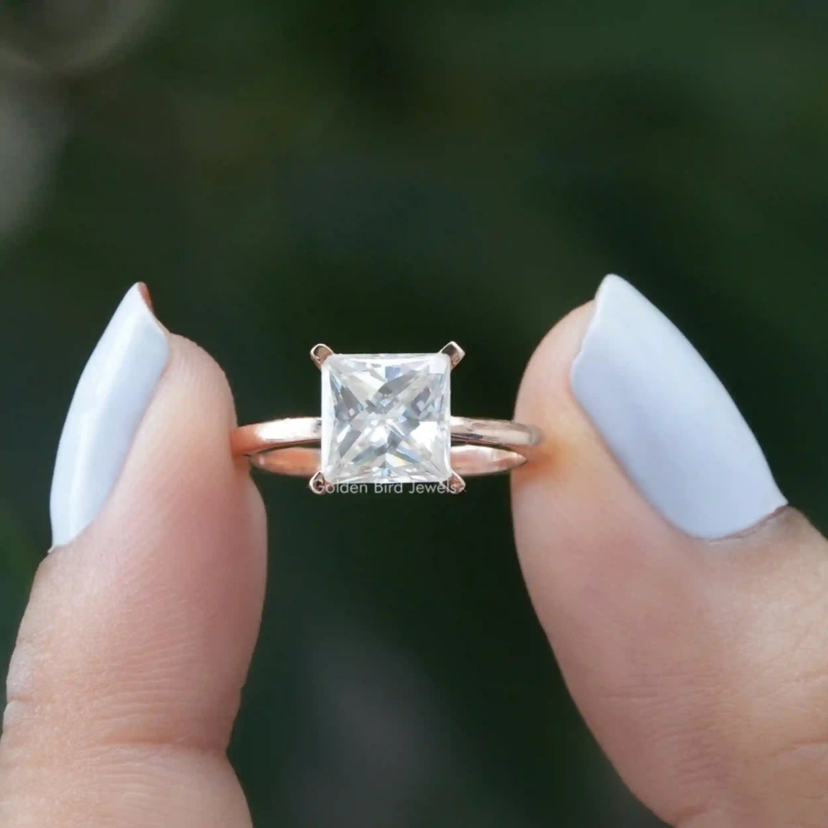 [In two finger front view of princess cut moissanite ring in 14k yellow gold]-[Golden Bird Jewels]