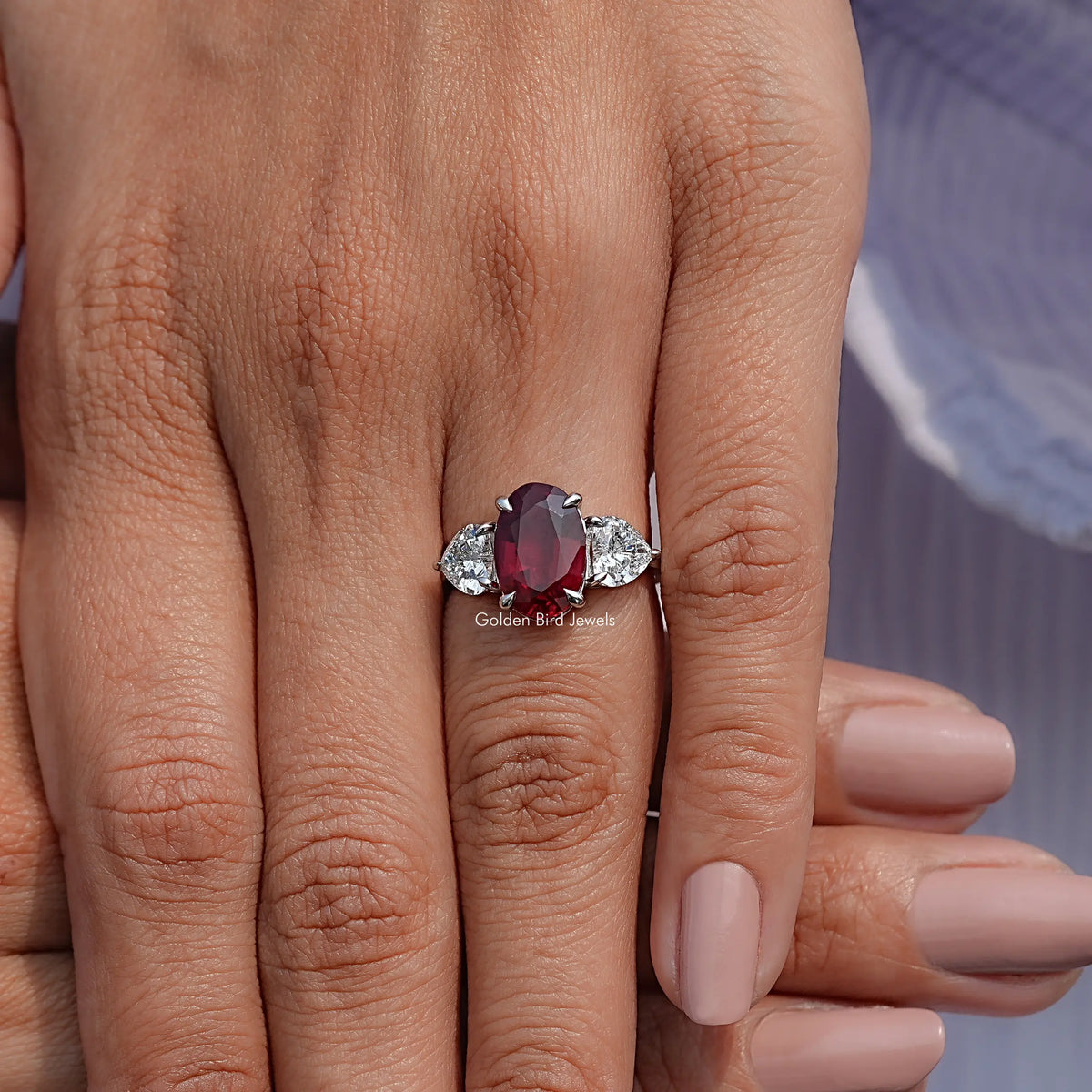 Three-stone oval ruby ring on finger with red center and white side stones
