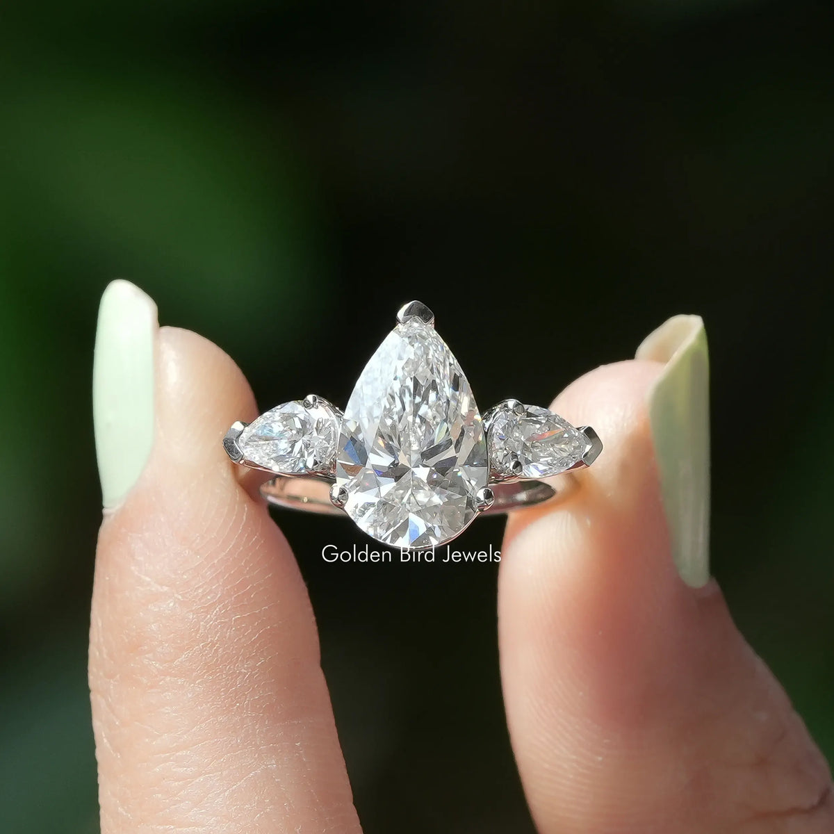 Two fingers holding the Pear Cut Three Stone Diamond Engagement Ring