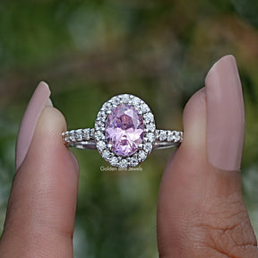 Front View of A Pink Tourmaline Oval Cut Gemstone Halo Ring In two fingers