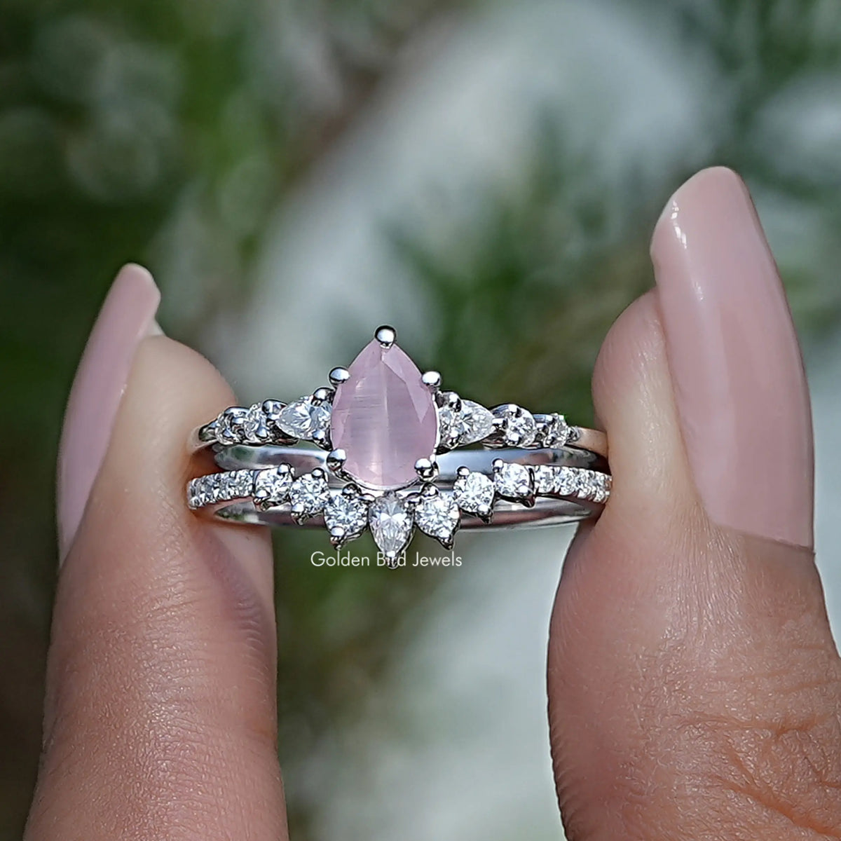 Two fingers holding the Pink Pear Cut Gemstone Bridal Ring Set