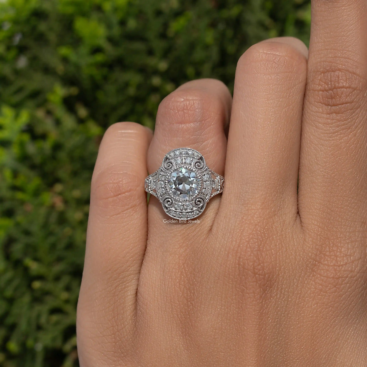 Sterling silver vintage round moissanite ring with ornate halo, on finger