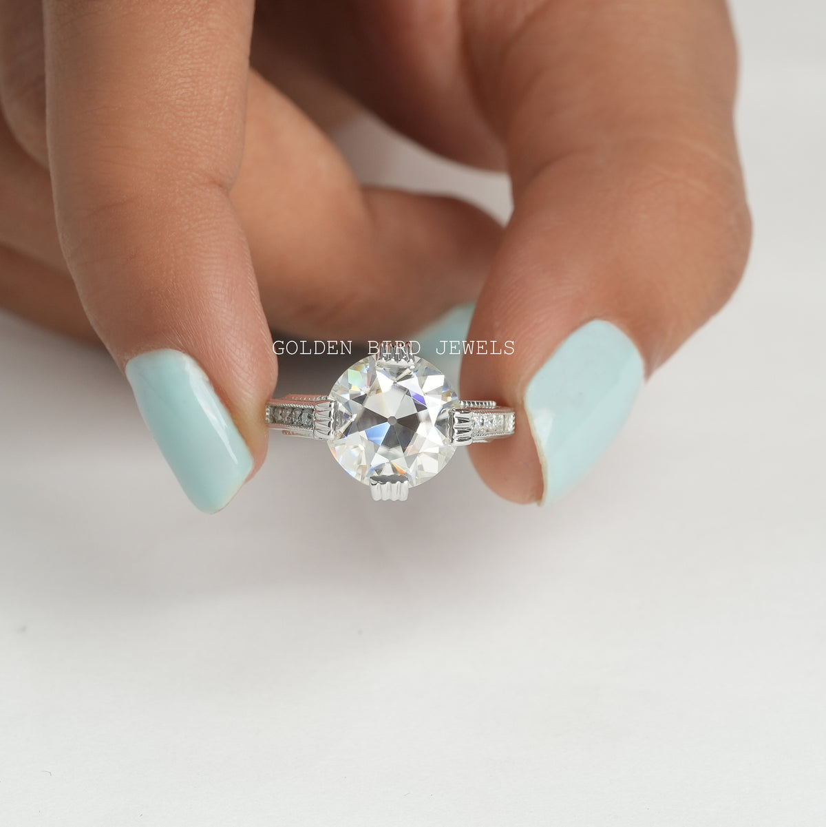 [ A woman's hand holding a moissanite ring with a colorless round cut stone]-[Golden Bird Jewels]