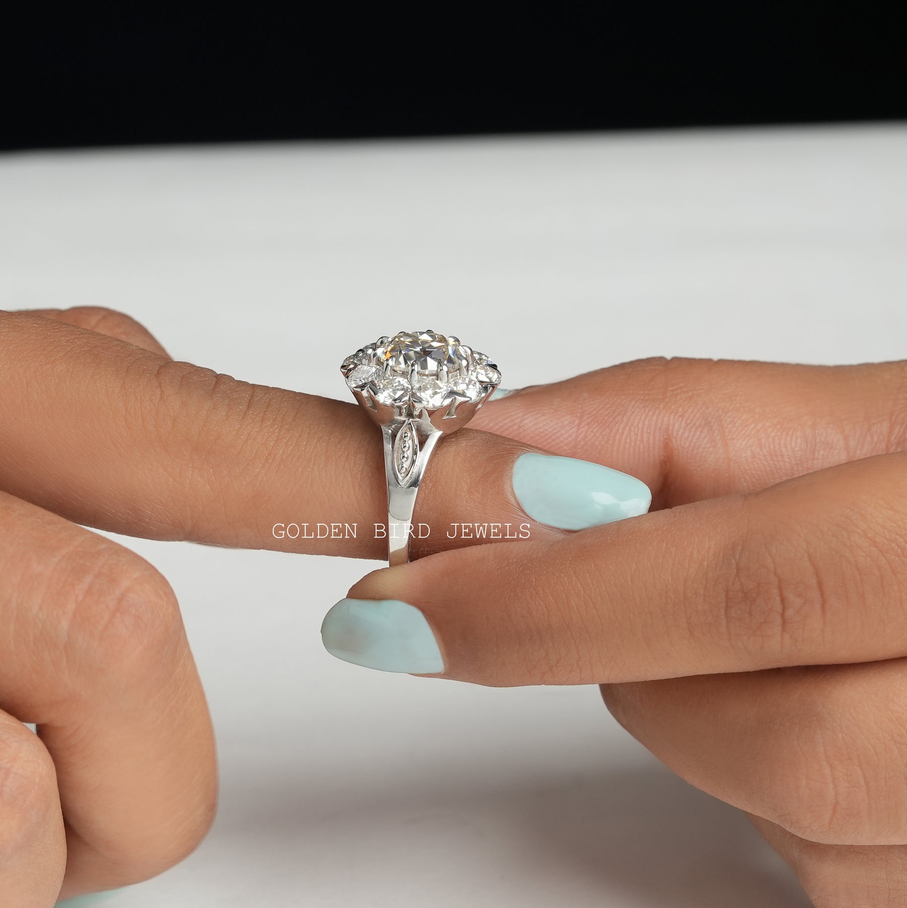 [A woman's hand holding a moissanite halo engagement ring]-[Golden Bird Jewels]