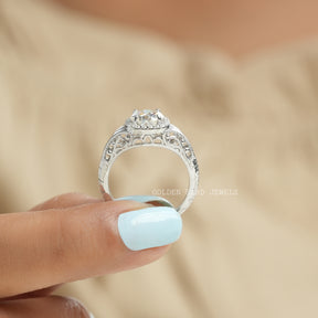 [Two finger front view of halo moissanite round cut ring set in 4 prongs]