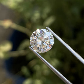 Front view of the Tweezers Holding Colorless Round Cut Loose Moissanite Stone In White