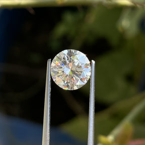 Front view of the Tweezers Holding Heart And Arrow Round Cut Loose Moissanite Stone In White